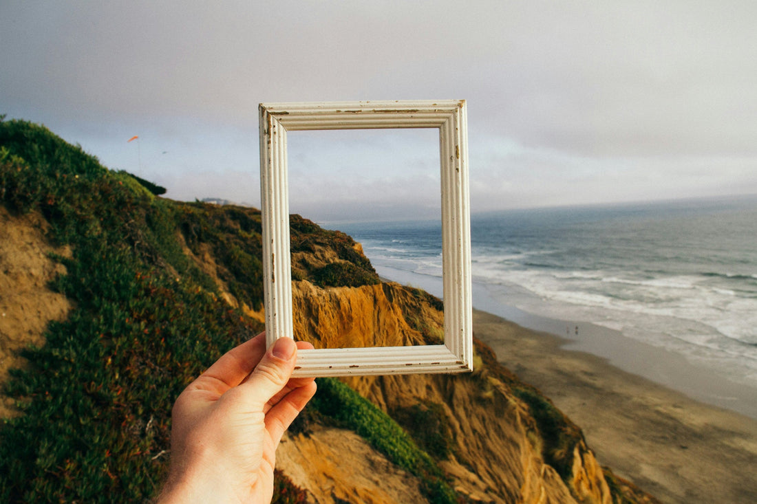 une main tient un cadre vide devant un paysage